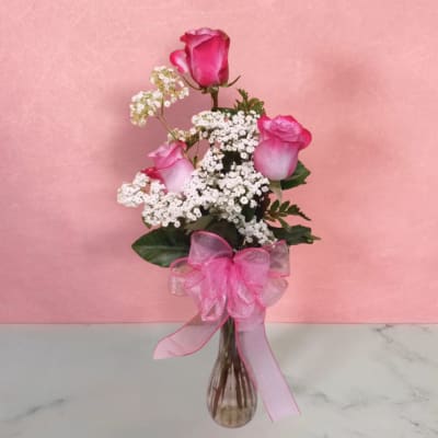 Pink roses with white filler flowers in a glass vase with a pink ribbon