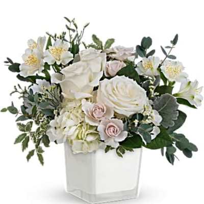 White roses and pale pink flowers in a clear square vase