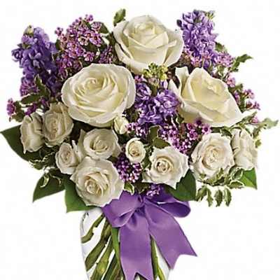 White roses and purple flowers arranged in a glass vase with a purple ribbon.