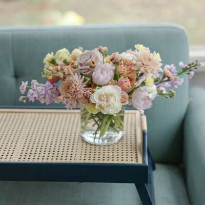 Pastel mixed flower bouquet in a clear glass vase on a tray table