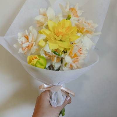 Handheld bouquet of yellow and white flowers wrapped in white paper