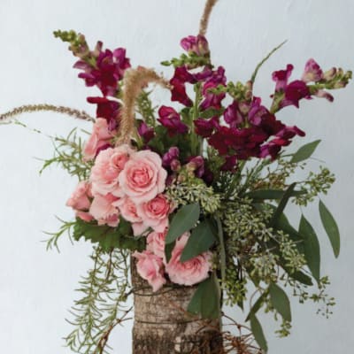 Pink roses and magenta snapdragons in a rustic bark container