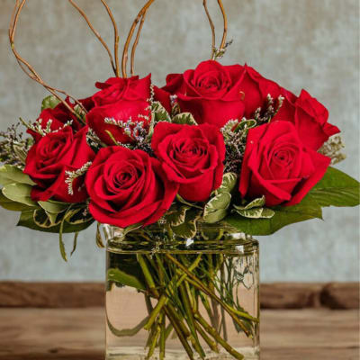 Red roses arranged in a clear glass vase with heart-shaped twigs