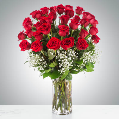 Tall bouquet of red roses in a clear glass vase with white baby's breath