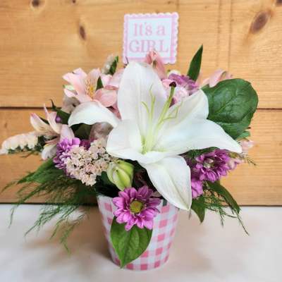 Pink and white flower arrangement in a checkered container with an "It's a Girl" sign
