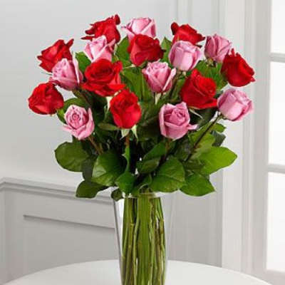 Tall bouquet of red and pink roses arranged in a clear glass vase on a white table