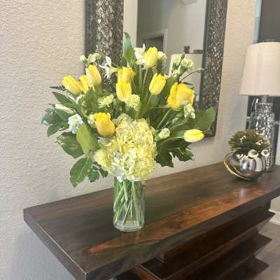 Yellow tulips, roses, and hydrangeas in a clear glass vase on a wooden console table