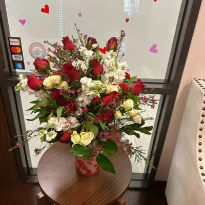 Tall arrangement of red roses, white flowers, and cream spray roses in a patterned ceramic vase