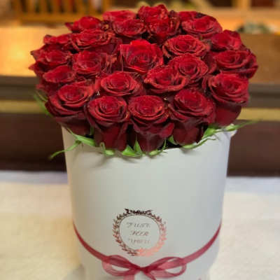 Red roses arranged in a white hat box with a pink ribbon