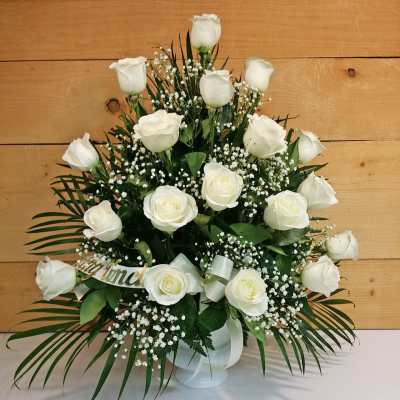 White roses arranged in a vase with baby's breath and palm fronds