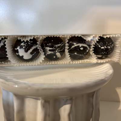 Box of five dark chocolate truffles with white splatter decoration on a white pedestal