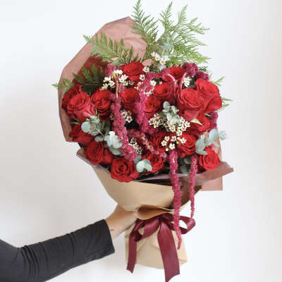 Bouquet of red roses with pink filler and greenery wrapped in paper