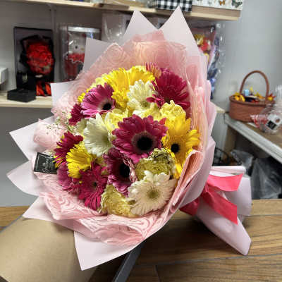 Bouquet of pink, yellow, and white gerbera daisies wrapped in pink paper