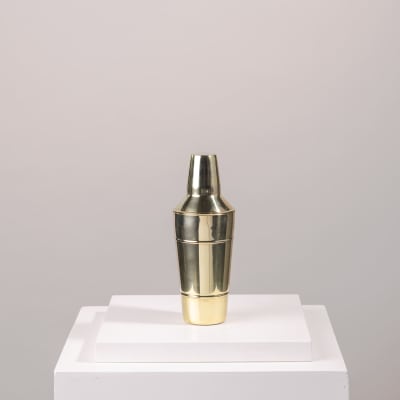 Gold metal cocktail shaker on a white pedestal