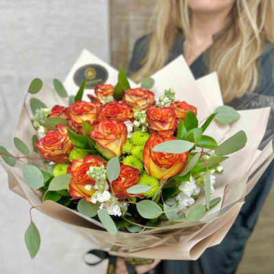 Bouquet of orange and yellow roses with green mums and white blooms wrapped in beige paper
