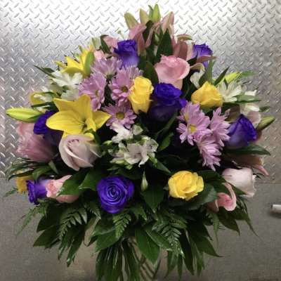 Mixed bouquet of lilies, roses, and daisies in a clear glass vase