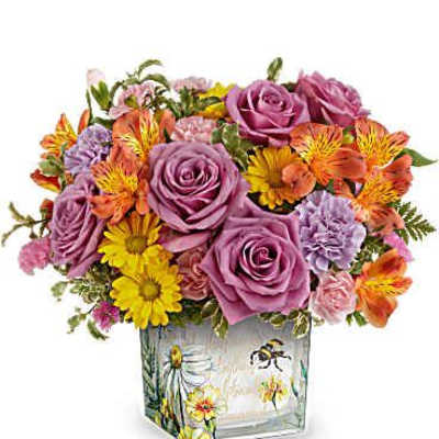 Square vase of purple roses with orange alstroemeria, yellow daisies, and pink blooms in a floral printed container