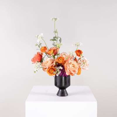 Peach and orange flower arrangement in a black vase
