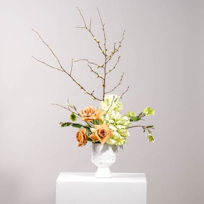 Peach roses and white-green flowers in a white vase with bare branches