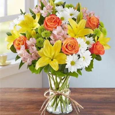 Bouquet of yellow lilies, orange roses, and white daisies in a glass vase