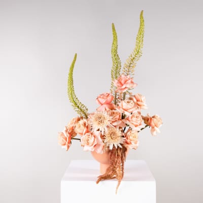 Peach roses and pale blooms in a peach vase with tall green spikes
