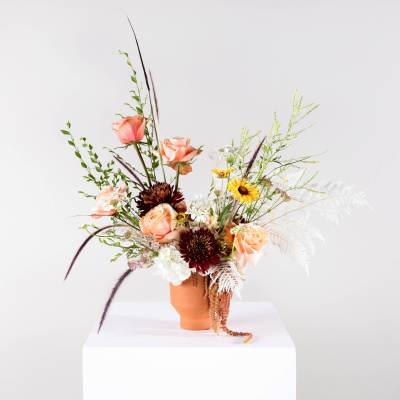 Mixed bouquet with peach roses and dark blooms in a terracotta vase