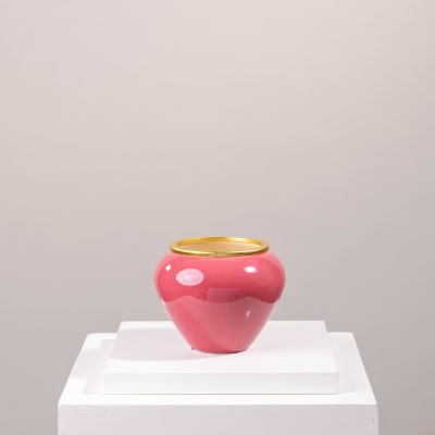 Pink ceramic vase with a gold rim on a white pedestal