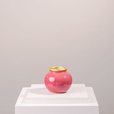 Pink ceramic vase with a gold rim on a white pedestal