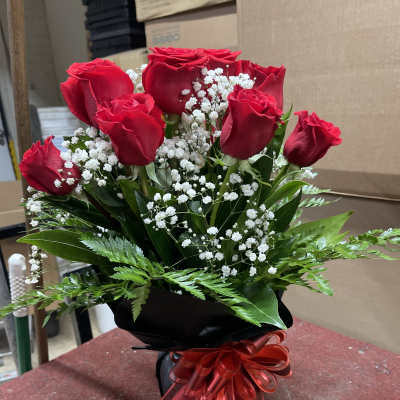 Red roses with white baby's breath in a black wrapped bouquet tied with a red ribbon
