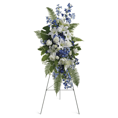 Standing floral spray with white lilies, blue flowers, and ferns on an easel