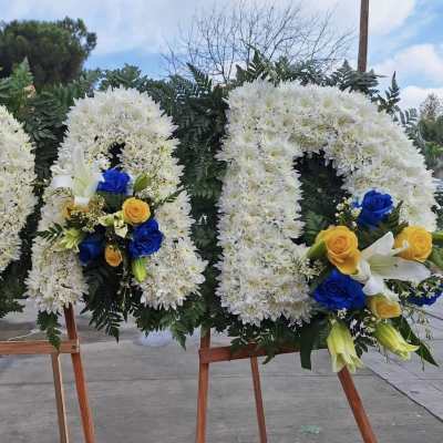 Three large white floral wreaths on wooden easels with blue and yellow roses