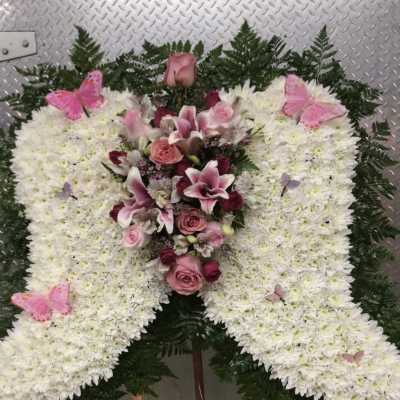 Large white floral funeral spray with pink roses and lilies on an easel