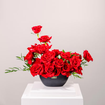 Red roses arranged in a black vase on a white pedestal