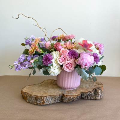 Pink and purple floral arrangement in a ribbed vase on a wood slab