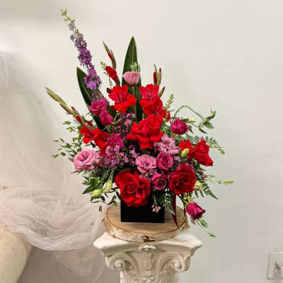 Tall arrangement of red and pink flowers in a black container
