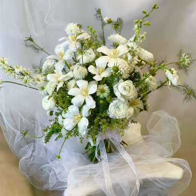 White floral bouquet with lilies and ranunculus tied with a sheer ribbon