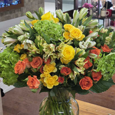 Bouquet of yellow and orange roses with green hydrangeas in a glass vase