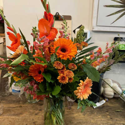 Orange mixed flower arrangement in a clear glass vase