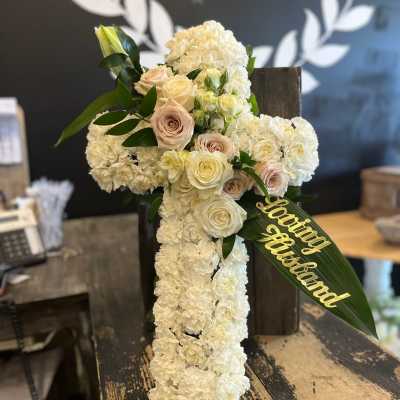 White floral cross arrangement with pale roses and a gold "loving husband" ribbon