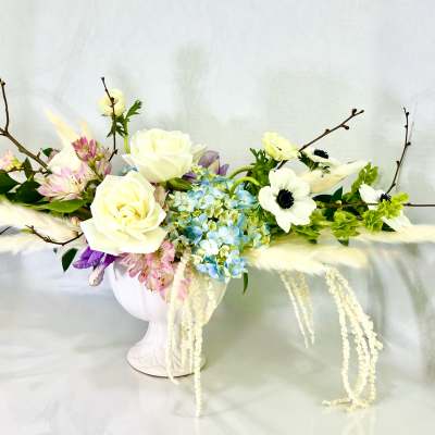 White roses and blue hydrangeas in a white vase with branches and feathers