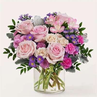 Pink roses and purple flowers arranged in a clear glass vase