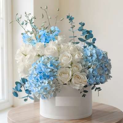 White roses and blue hydrangeas arranged in a white box