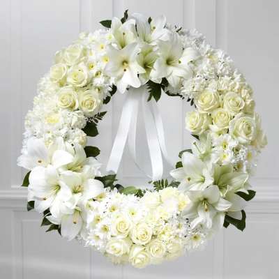 White floral wreath with roses and lilies tied with a ribbon