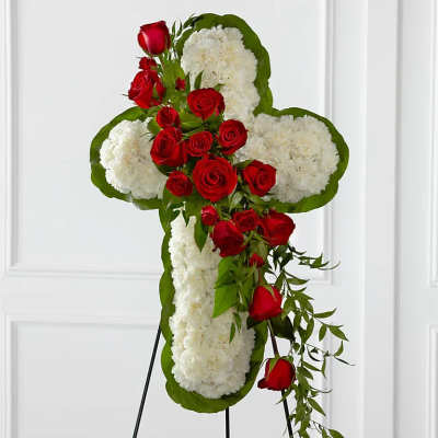 Cross-shaped floral tribute with red roses and white flowers on a stand