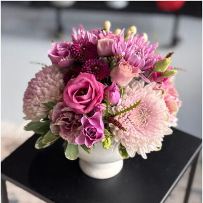 Compact arrangement of pink and purple roses and mums in a white ceramic vase