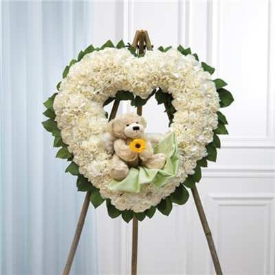 Heart-shaped white floral wreath with a teddy bear and ribbon on an easel