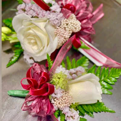 Two small floral corsages with white roses and pink ribbons
