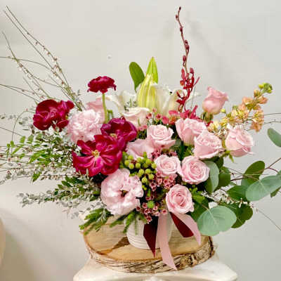 Pink and red floral arrangement in a white container with lilies and roses