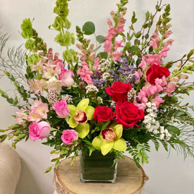 Mixed bouquet in a square glass vase with pink, red, and green flowers