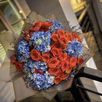Bouquet of orange roses and blue hydrangeas wrapped in tan paper